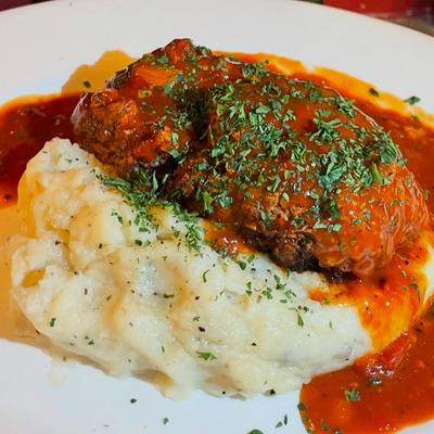 Meatloaf topped with red sauce and herbs, served over mashed potatoes.
