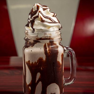 Chocolate Milkshake served in a mason jar mug, topped with whipped cream and chocolate sauce.