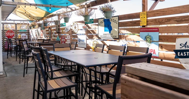 Outdoor patio with tables, chairs, shade sails, string lights and decorative signs