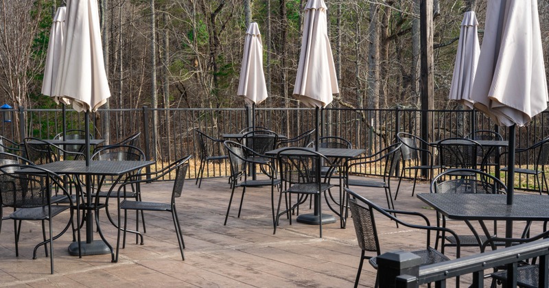 Outdoor seating area with metal tables and chairs, topped by closed parasols