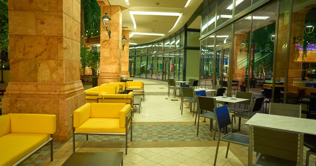 Café seating area - yellow lounge chairs, dark tables, glass walls, tan stone columns, plants.
