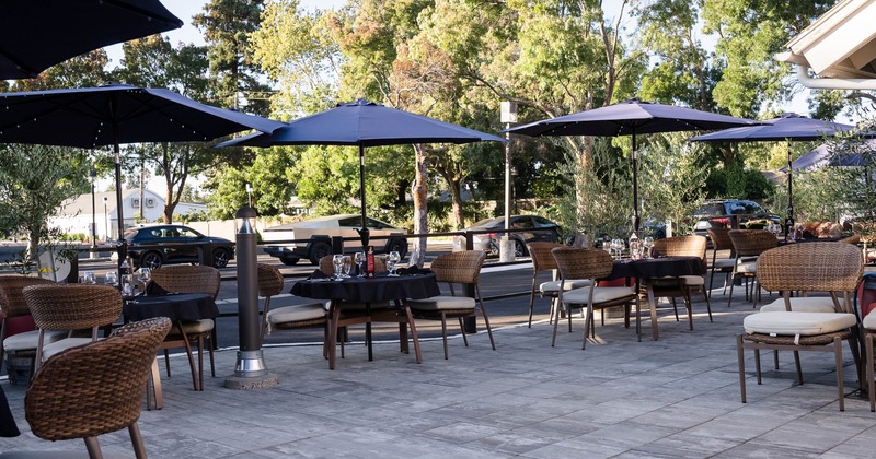 Outdoor patio - shaded tables, wicker chairs, and place settings beneath large dark umbrellas.