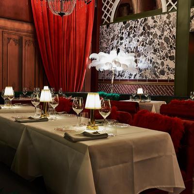 Interior with tables set for dining, red velvet curtains and crystal chandeliers.