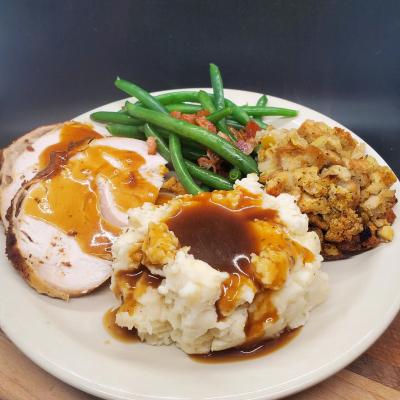 Sliced turkey with gravy, mashed potatoes, stuffing, and green beans with bacon.