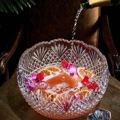 A crystal punch bowl being filled with a sparkling wine, and garnished with fruit and flowers.