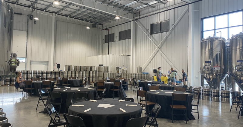 Interior, area with tables and chairs, surrounded by brewery tanks and kegs