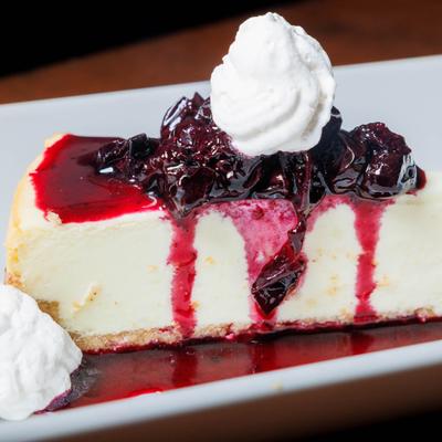 Cheesecake slice topped with dark berry compote and whipped cream.