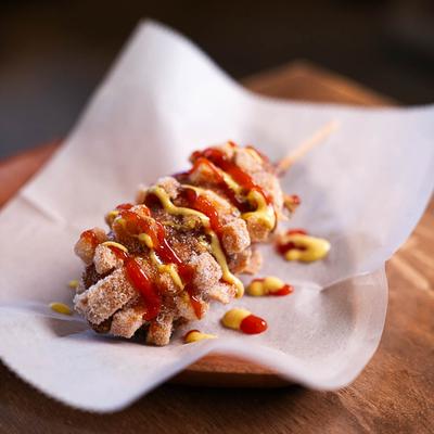 Mozzarella-stuffed potato corn dog, drizzled with mustard and ketchup.