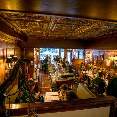 Crowded restaurant dining room beneath ornate ceiling.