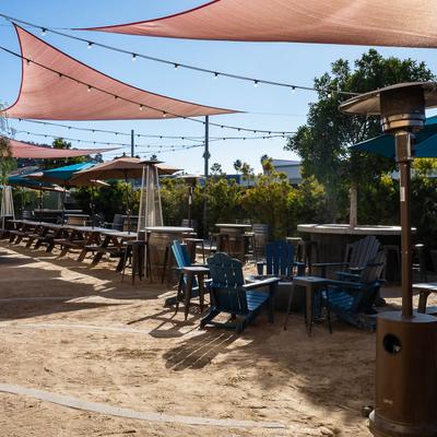 Outdoor seating area on the sand with tables, sunshades, string lights, and greenery.