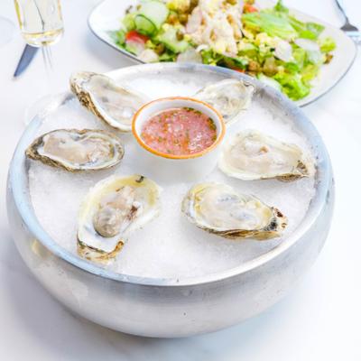 Raw oysters served on a bed of ice with a small bowl of red onion mignonette.