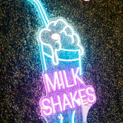 Neon sign in the shape of a milkshake glass against a green wall.