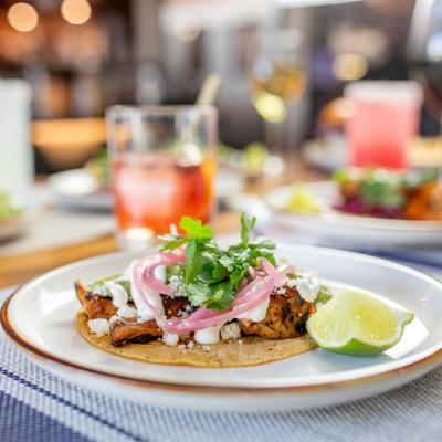 Taco with grilled meat, pickled onions, and a lime wedge.