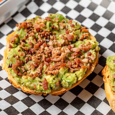 Avocado bagel toast topped with bacon bits, close-up.