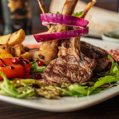 Grilled lamb chops garnished with red onion rings, served with potatoes and vegetables.