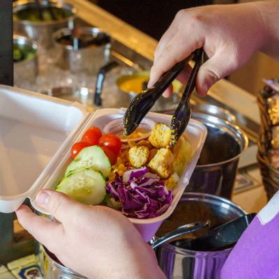 A person holding a foam container filled with cucumbers, red cabbage, and croutons.