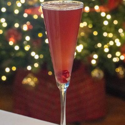 A red cocktail, set against a blurred background of Christmas tree lights.