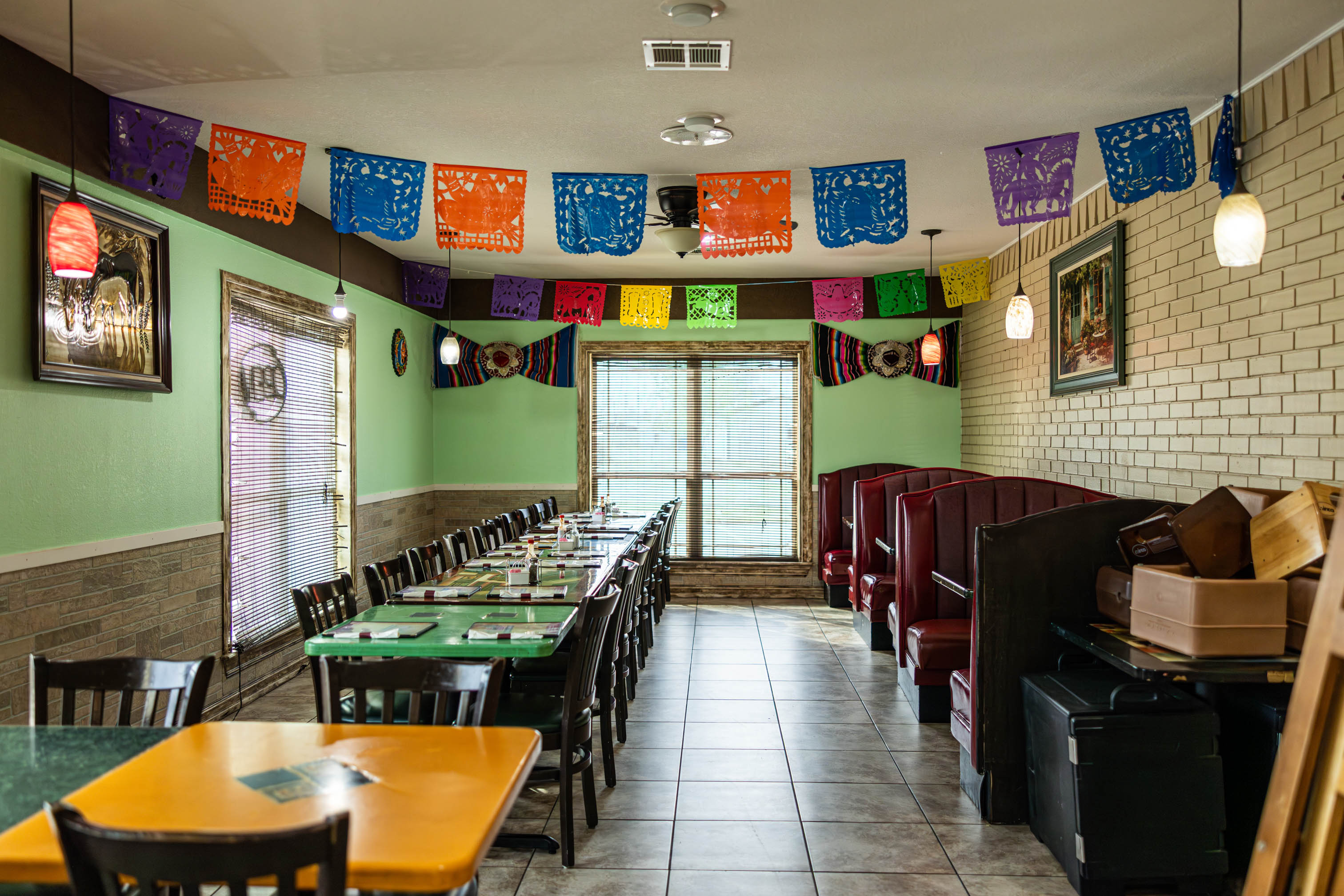 Empty Mexican restaurant dining room with tables, booth seating, and papel picado banners