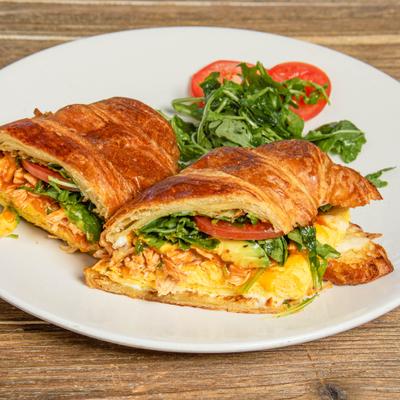 Croissant sandwich with eggs, cheese, greens and tomato, close up