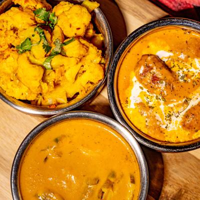 Yellow cauliflower dish served alongside two bowls of curry.