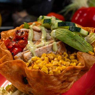 Chicken taco salad with avocado, corn, and cucumbers in a crispy tortilla bowl.
