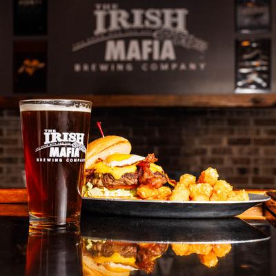 The Don Burger served with tater tots, accompanied with a glass of beer.