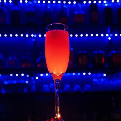 An orange drink in a flute glass with a blue-lit bar background.