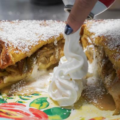 Whipped cream being sprayed onto a plate with an apple-stuffed French toast.