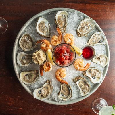 Overhead view of raw oysters on ice with shrimp, sauces, and lemon wedges.