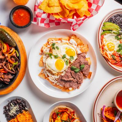 Chilaquiles topped with fried eggs and meat, surrounded by other Mexican dishes and chips.
