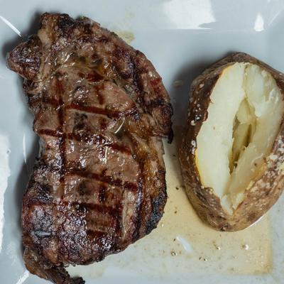 Overhead view of a plate with grilled rib eye steak and a baked potato.