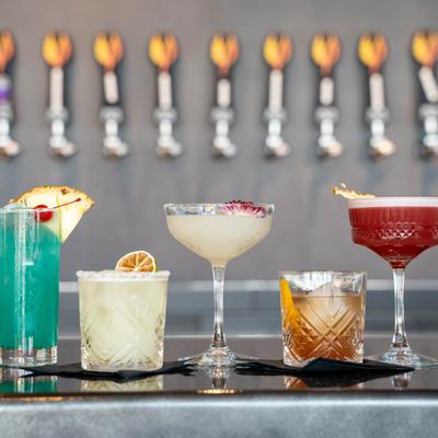 Selection of cocktails served on a bar counter with numerus tap handles in the background.