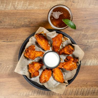 plate with chicken wings surrounding a ramekin of Ranch with a beer and a lime.