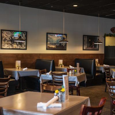 Restaurant dining area with checkered tablecloths, booth seating, and framed artwork on the walls.