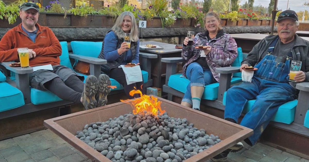 People sitting around a fire pit drinking beers on the outdoor patio