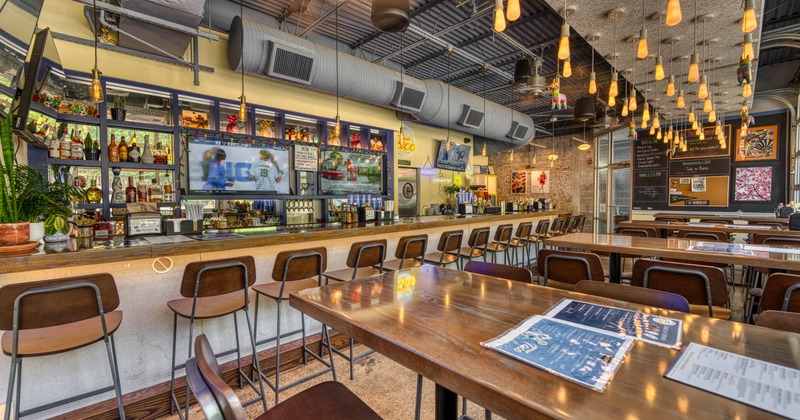 Modern interior - wooden tables, high stools, pendant lights and two TVs displaying sports.