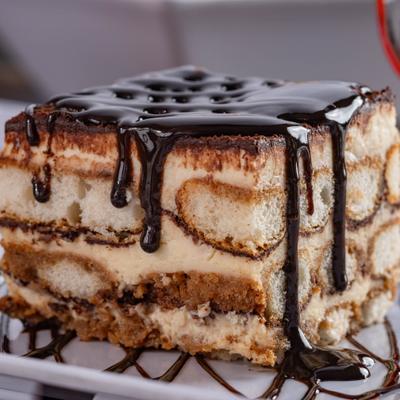 A slice of tiramisu topped with a chocolate drizzle.
