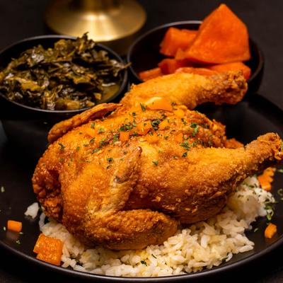 Fried Cornish Hen served on a bed of rice with collard greens and yams on the side.