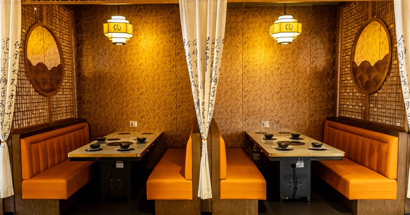 Interior with orange benches and hot pot tables, separated by a decorative curtain