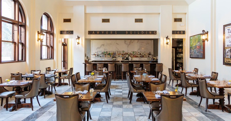 Bright dining room - leather chairs, set tables, arched windows and a central bar .