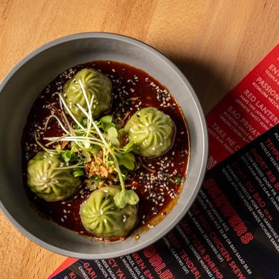 Veggie dumplings served in a dark sauce, garnished with sesame seeds and microgreens.