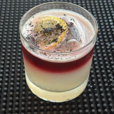 Blood on The Water drink with a white base and red top, garnished with a lemon slice.
