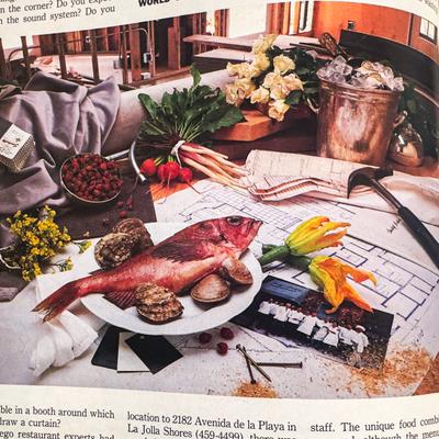 Assorted produce on a table with a hammer, flowers, and architectural plans