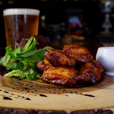 BBQ  wings on a wooden board served with a salad and a beer.