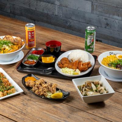 Various dishes served on the table with two canned drinks.