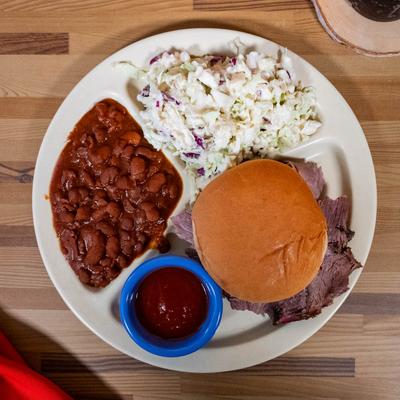 Brisket sandwich served with sides of baked beans, coleslaw, and BBQ sauce.