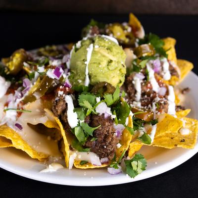 Nachos topped with melted cheese, beef, guacamole, sour cream, jalapenos, red onions, and cilantro.
