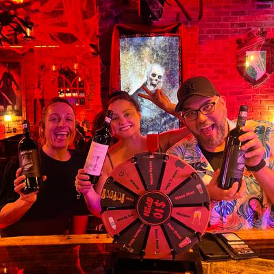 Three people smiling behind a prize wheel while holding bottles together.