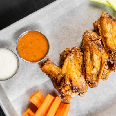 A plate of fried chicken wings with carrot sticks and dipping sauce.