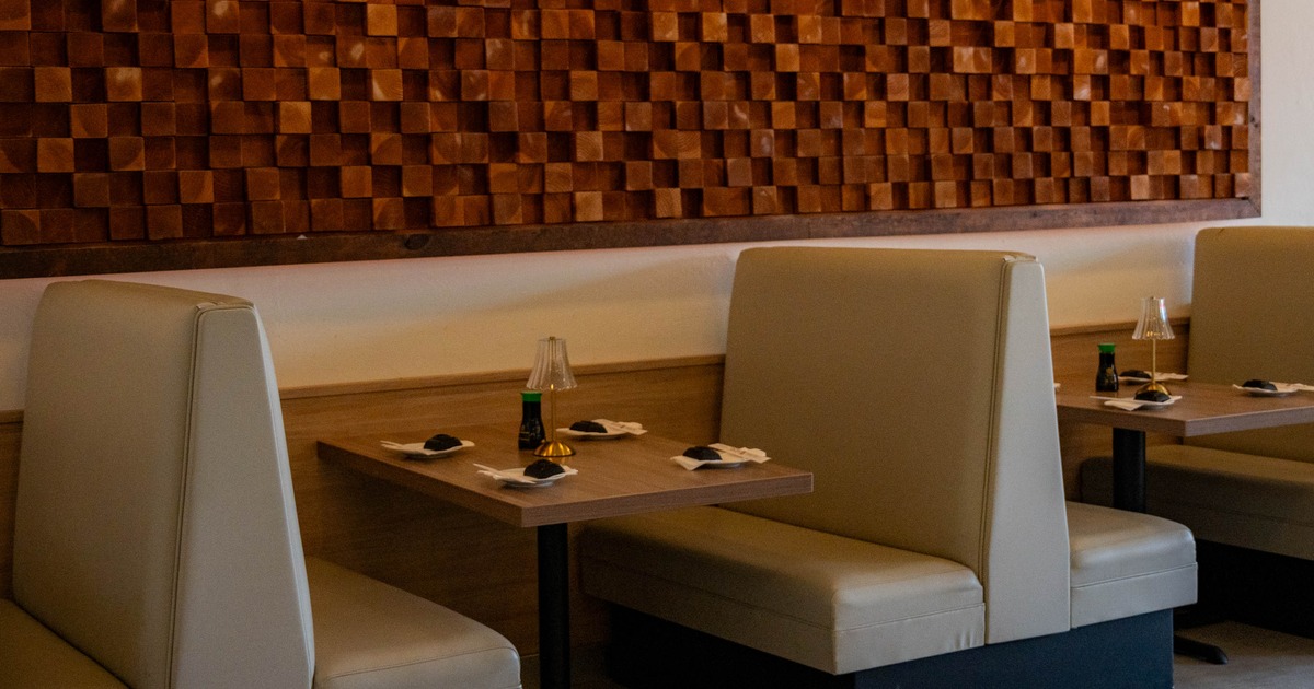 Interior of a restaurant featuring two light-colored booths, a wooden table with items